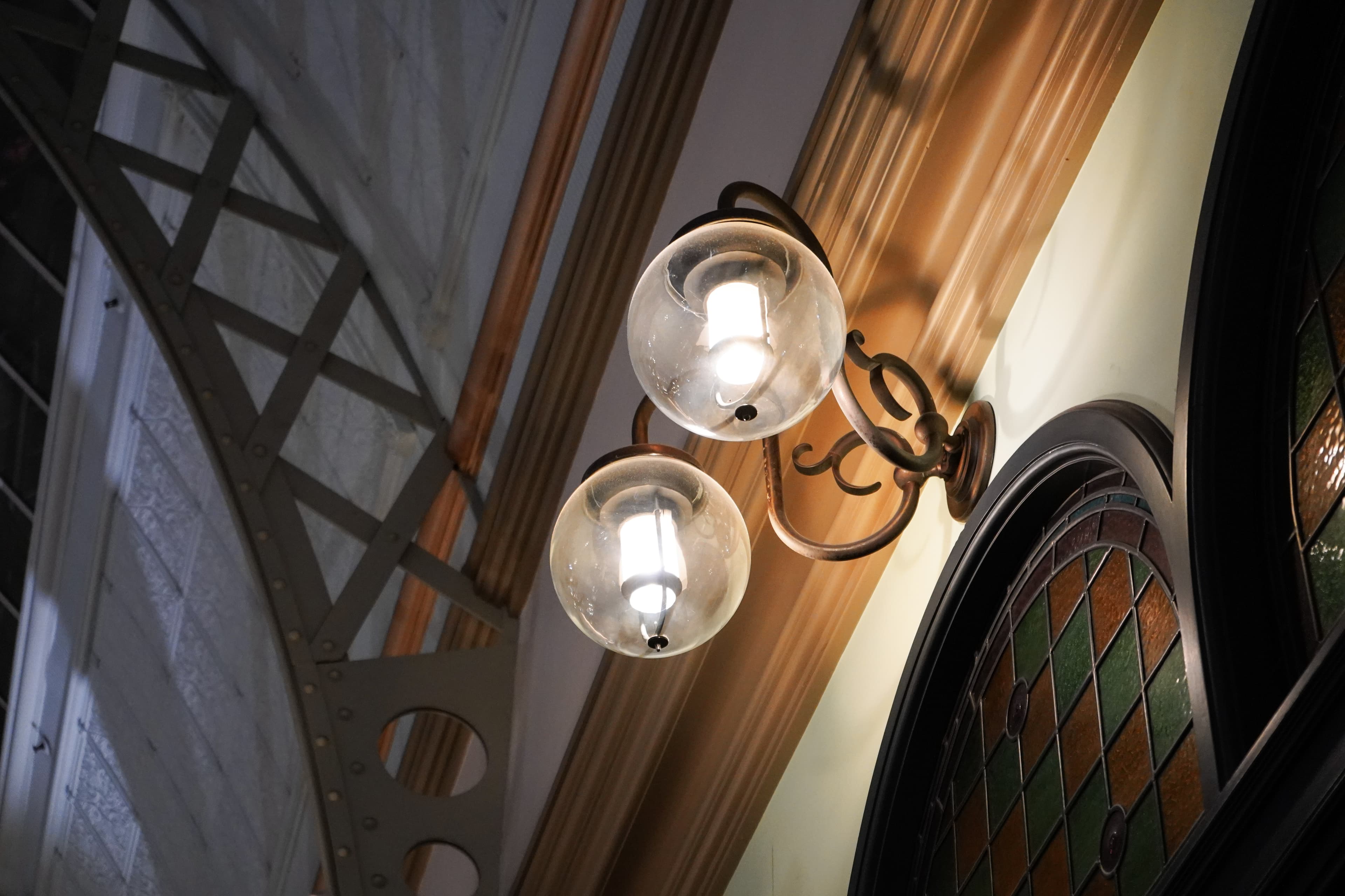Two glowing glass lamps beside stained-glass windows and steel roof beams